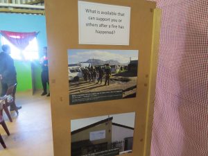 A notice is pinned to a board with two photos below it. The notice says, "What is available that can support you or others after a fire has happened?". One photo shows people, the other a building.
